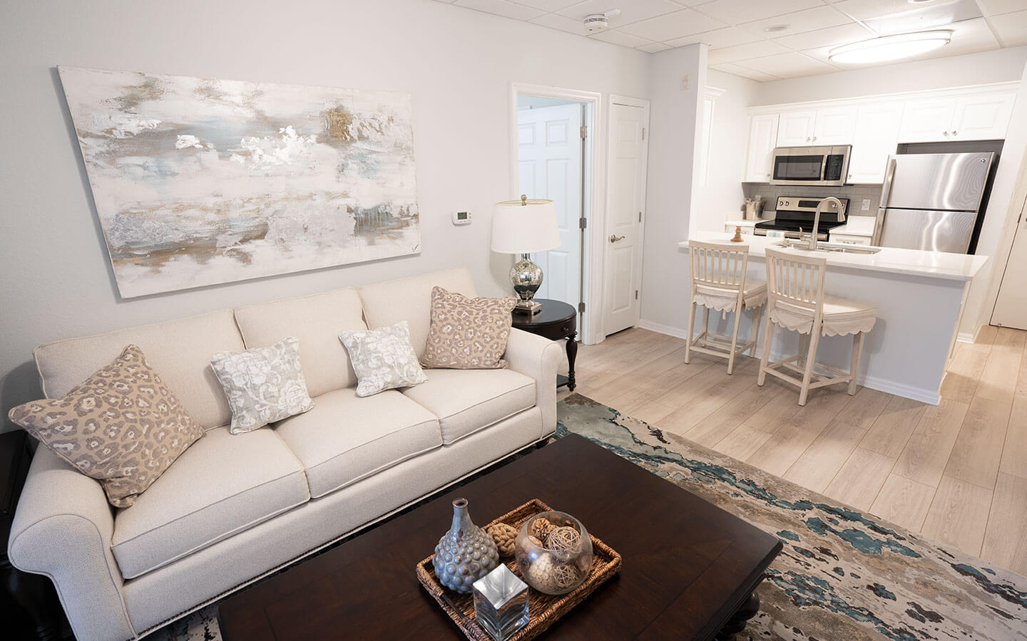 View of the living room with large couch and kitchen with two bar stools at the sink counter.